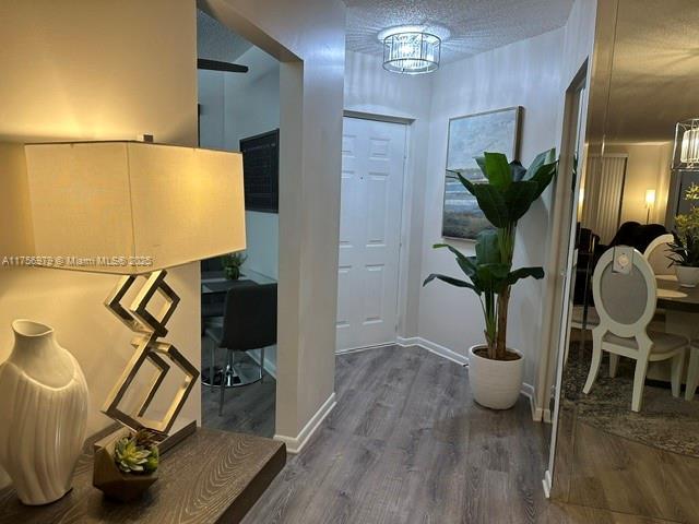 entryway with an inviting chandelier, a textured ceiling, baseboards, and wood finished floors