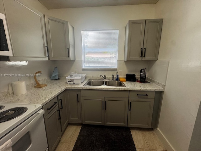 kitchen with white range with electric cooktop, gray cabinets, a sink, and baseboards