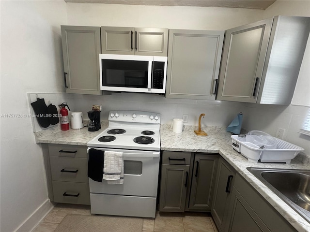 kitchen with white electric stove, gray cabinetry, a sink, baseboards, and light stone countertops