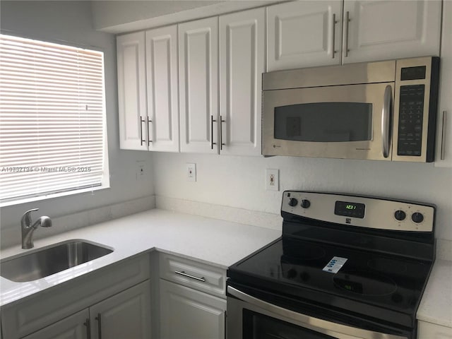 kitchen featuring stainless steel appliances, light countertops, white cabinetry, and a sink