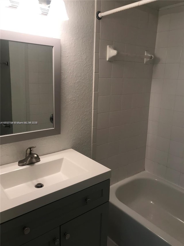 full bathroom featuring  shower combination, a textured wall, and vanity