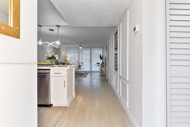 kitchen featuring a textured wall, white cabinetry, a textured ceiling, light wood-type flooring, and dishwasher