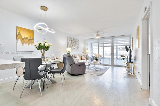 interior space featuring expansive windows, light wood-style flooring, baseboards, and ceiling fan with notable chandelier