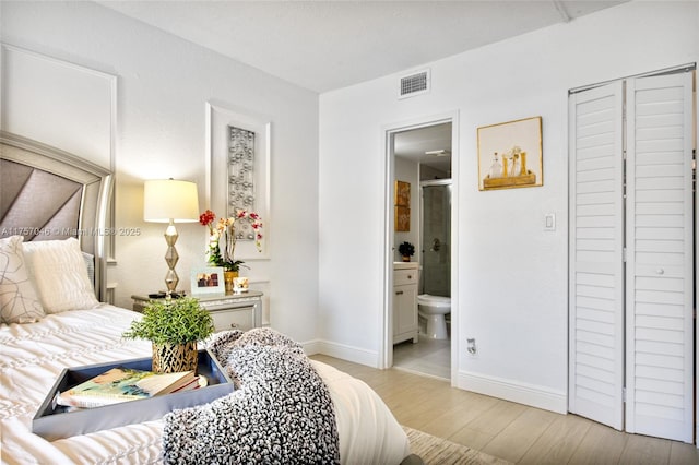 bedroom with ensuite bathroom, wood finished floors, visible vents, and baseboards