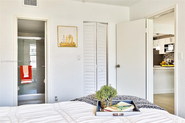 bedroom with ensuite bath, visible vents, and wood finished floors