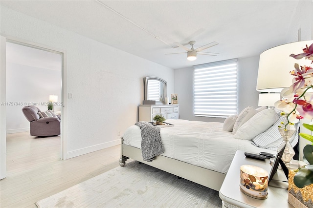 bedroom featuring ceiling fan, a textured wall, wood finished floors, and baseboards