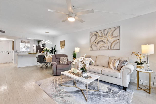 living area featuring visible vents, baseboards, light wood-style flooring, and a ceiling fan