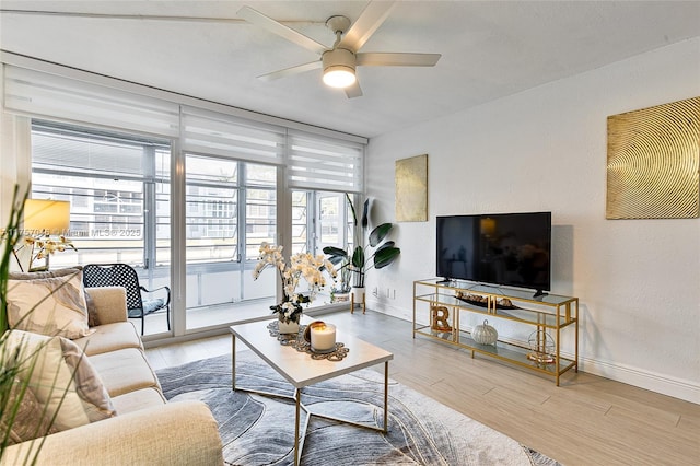 living room with a wall of windows, a ceiling fan, baseboards, and wood finished floors