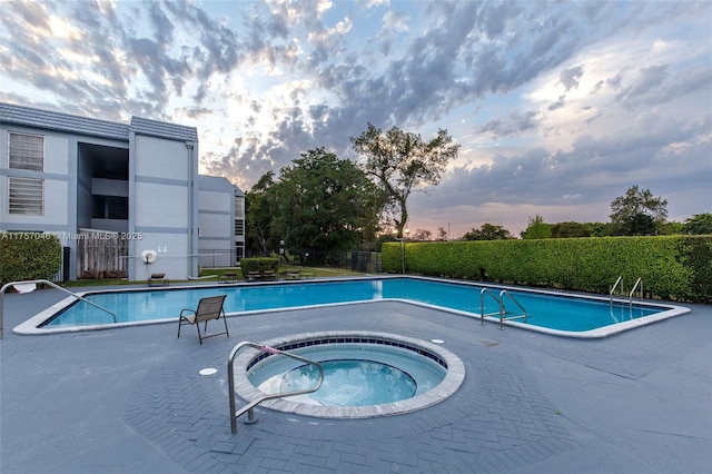 pool at dusk featuring a community hot tub, fence, and a community pool