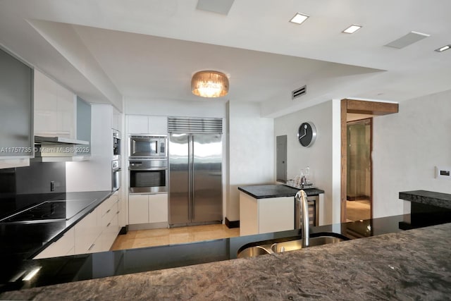 kitchen with built in appliances, a sink, visible vents, and white cabinets