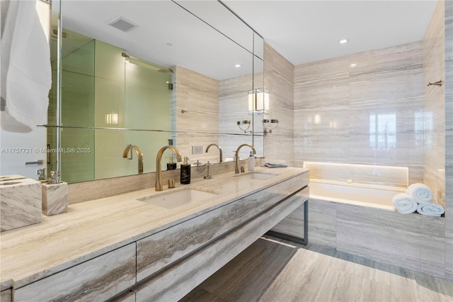 full bathroom with double vanity, a bathtub, a sink, and tile walls