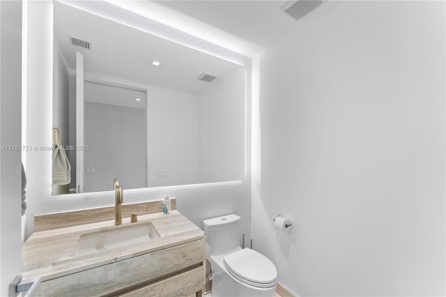 bathroom with toilet, vanity, and visible vents