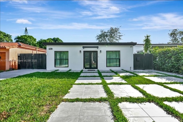 view of front of home with stucco siding, fence, a front lawn, and french doors