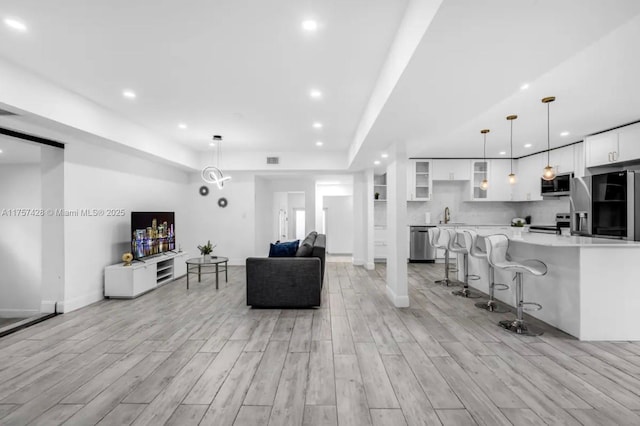 living area featuring wood finish floors, a tray ceiling, recessed lighting, visible vents, and baseboards