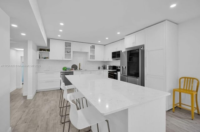 kitchen with stainless steel appliances, a breakfast bar, light wood finished floors, and recessed lighting