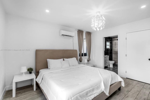 bedroom featuring a wall unit AC, recessed lighting, ensuite bath, light wood-type flooring, and baseboards