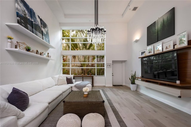 living room featuring a tray ceiling, visible vents, a high ceiling, and an inviting chandelier