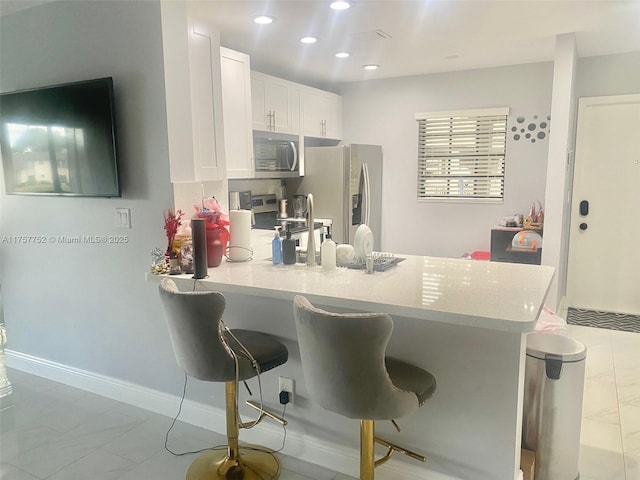 kitchen featuring stainless steel appliances, white cabinetry, a peninsula, and a kitchen bar