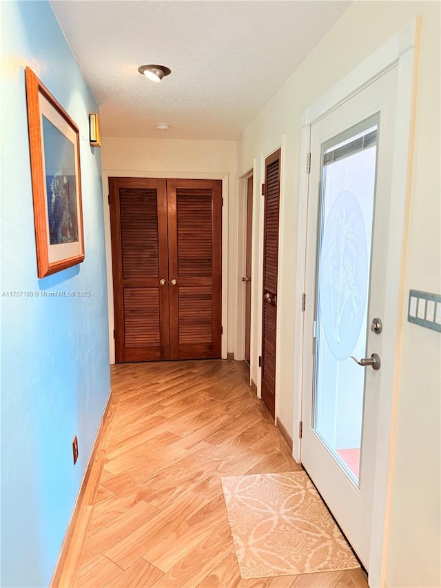 hallway with a textured ceiling, light wood-type flooring, and baseboards