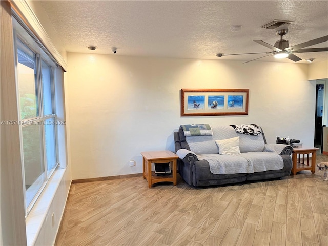 living area with visible vents, baseboards, light wood-style floors, a textured ceiling, and a ceiling fan