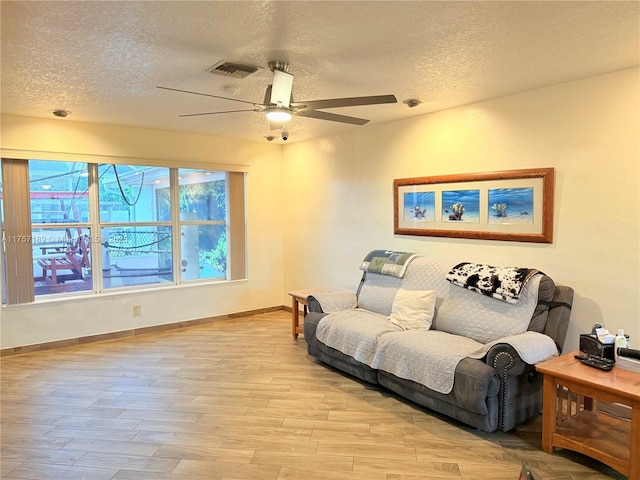living room with visible vents, light wood-style floors, a ceiling fan, and a textured ceiling