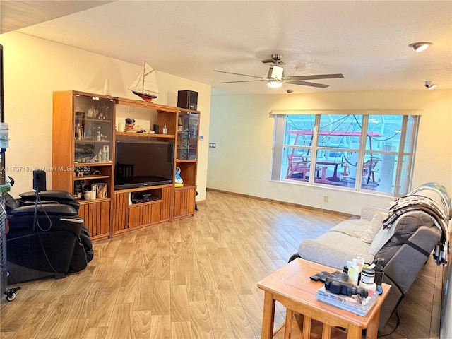 living room featuring a textured ceiling, light wood-style flooring, baseboards, and ceiling fan