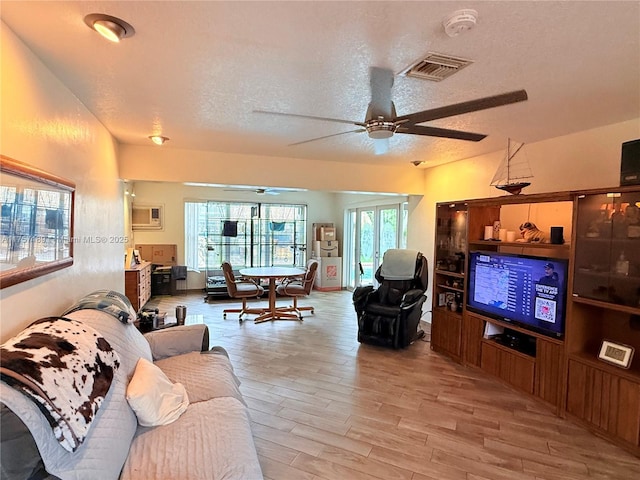 living room with light wood-style flooring, a ceiling fan, visible vents, and a textured ceiling