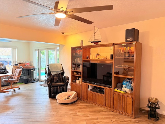living room with a ceiling fan, light wood finished floors, and a textured ceiling