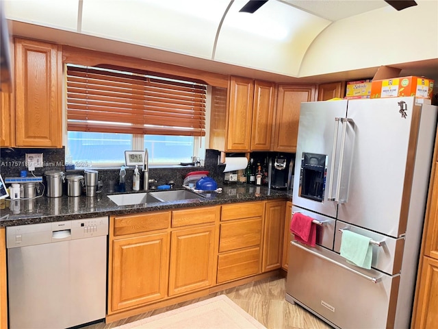 kitchen featuring brown cabinets, vaulted ceiling, a sink, dishwasher, and stainless steel fridge with ice dispenser