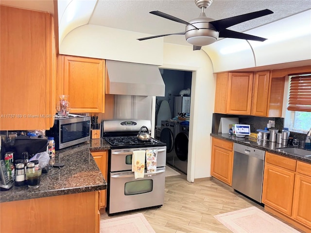 kitchen with a sink, ceiling fan, appliances with stainless steel finishes, washer and dryer, and wall chimney range hood