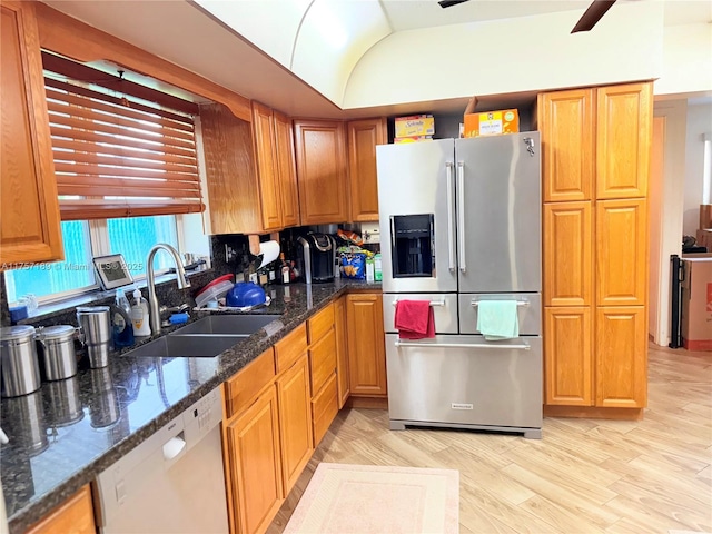 kitchen with a sink, dark stone countertops, appliances with stainless steel finishes, light wood finished floors, and lofted ceiling