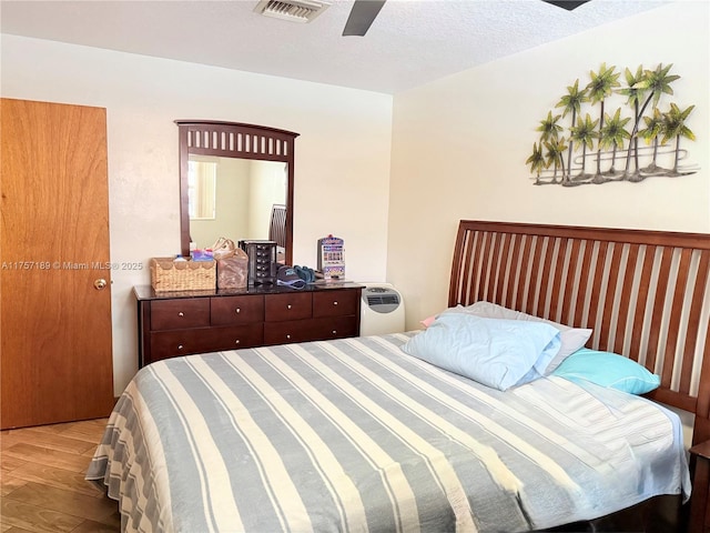 bedroom featuring a ceiling fan, a textured ceiling, visible vents, and wood finished floors