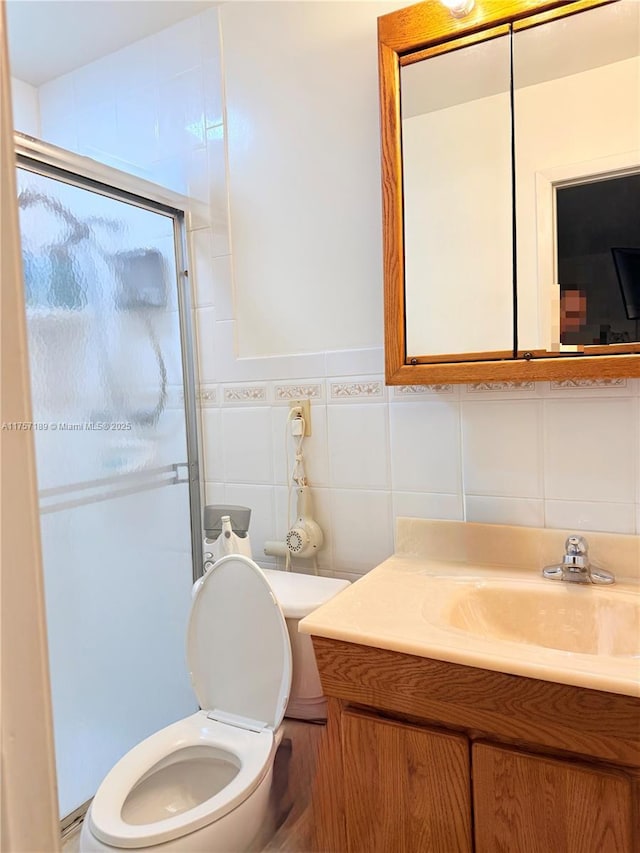 bathroom with tile walls, a shower stall, toilet, and vanity