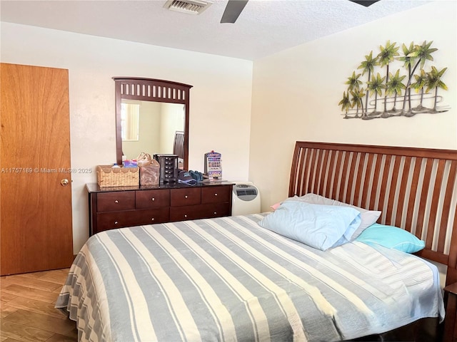 bedroom featuring visible vents, a textured ceiling, a ceiling fan, and wood finished floors