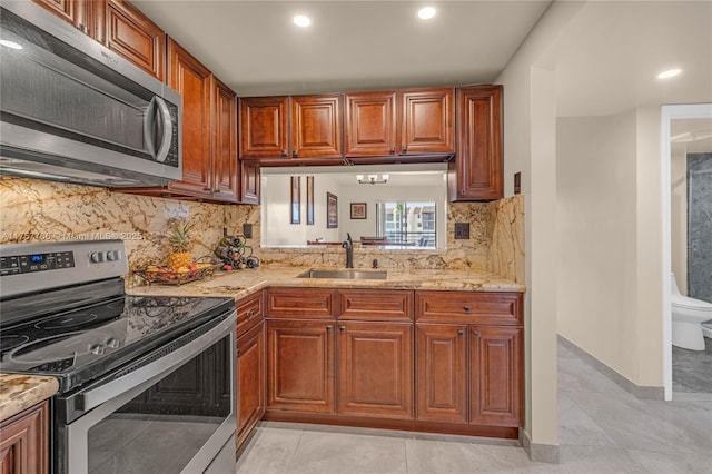 kitchen with light stone countertops, appliances with stainless steel finishes, brown cabinets, and a sink