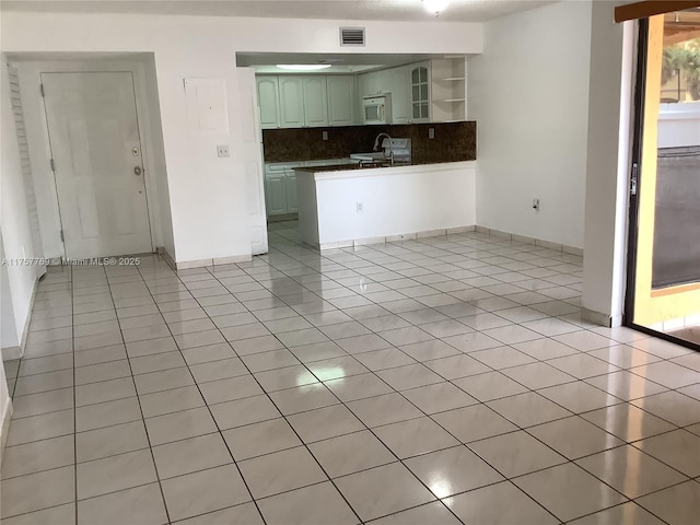 kitchen featuring light tile patterned floors, white microwave, visible vents, tasteful backsplash, and dark countertops