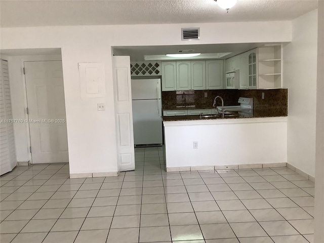 kitchen with light tile patterned floors, dark countertops, visible vents, white appliances, and a peninsula