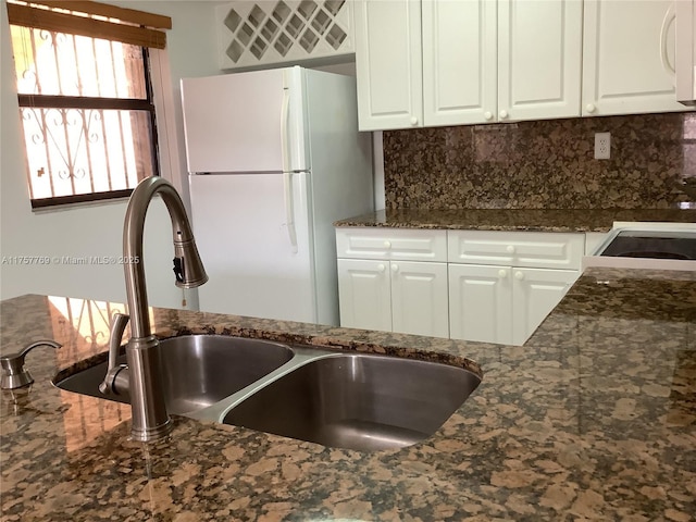 kitchen featuring white appliances, a sink, white cabinets, backsplash, and dark stone countertops