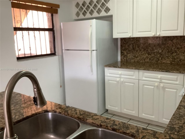 kitchen with white cabinetry, decorative backsplash, dark stone countertops, and freestanding refrigerator