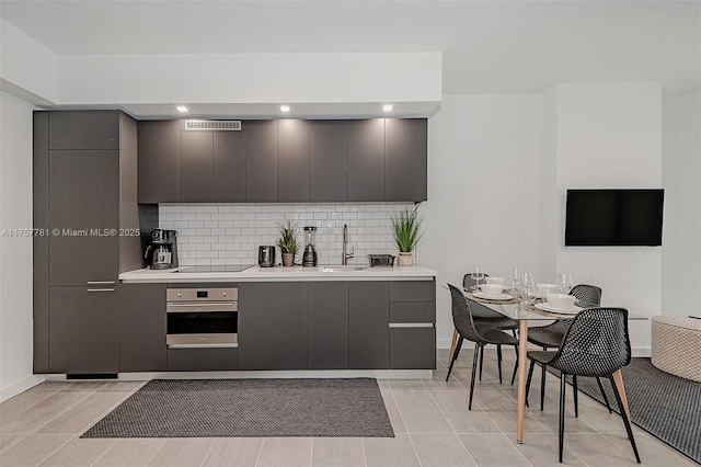 kitchen with black electric stovetop, oven, light countertops, tasteful backsplash, and modern cabinets