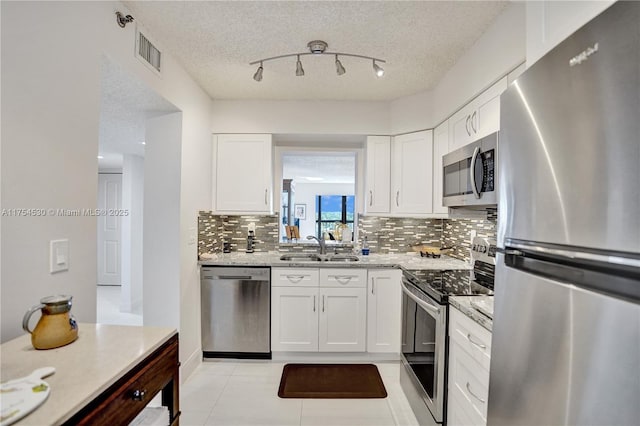 kitchen with stainless steel appliances, a sink, visible vents, white cabinetry, and decorative backsplash