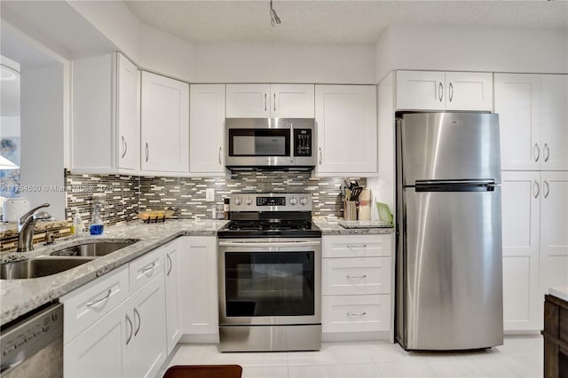 kitchen with appliances with stainless steel finishes, white cabinets, a sink, and tasteful backsplash