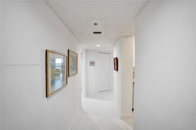 hall with visible vents, a textured ceiling, and baseboards