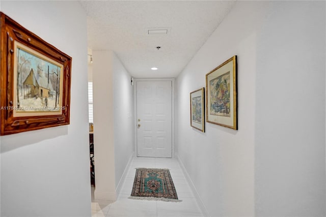 hallway with light tile patterned floors, baseboards, and a textured ceiling