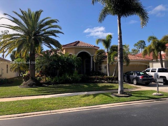 mediterranean / spanish house with stucco siding, an attached garage, driveway, a tiled roof, and a front lawn