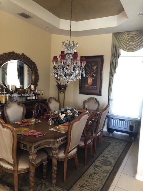 dining space with a chandelier, a tray ceiling, visible vents, and light tile patterned floors