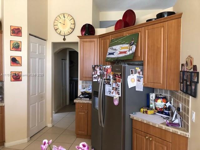 kitchen featuring light countertops, tasteful backsplash, light tile patterned flooring, and stainless steel fridge