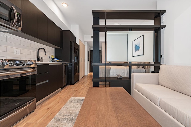 kitchen featuring stainless steel appliances, light wood-style floors, dark cabinets, and a sink