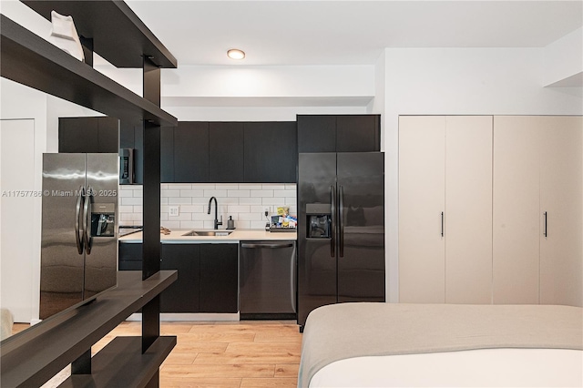 kitchen with a sink, dark cabinetry, dishwasher, stainless steel fridge with ice dispenser, and black fridge