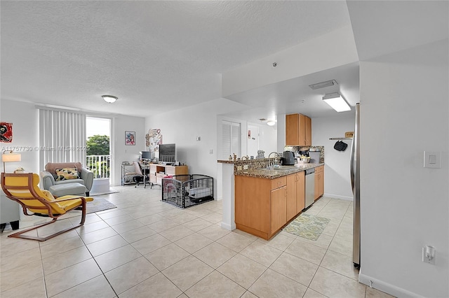 kitchen with light tile patterned floors, stone counters, a sink, open floor plan, and stainless steel dishwasher